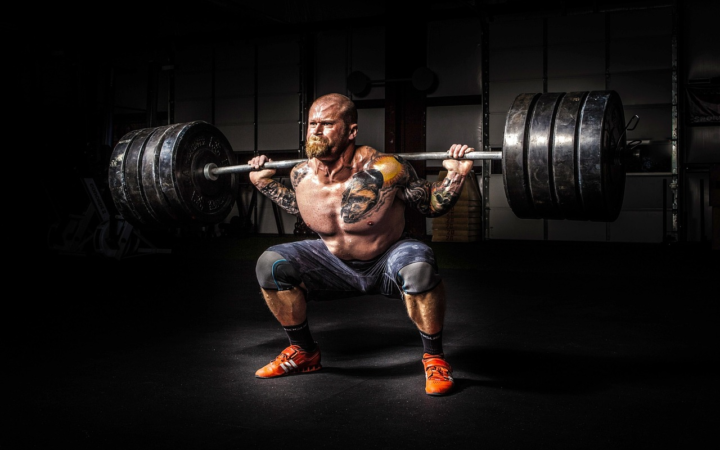 Hombre fuerte levantando pesas, con musculatura marcada y gesto de esfuerzo intenso durante un entrenamiento de fuerza.