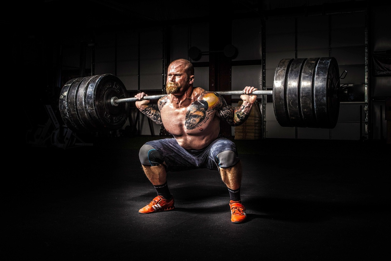 Hombre fuerte levantando pesas, con musculatura marcada y gesto de esfuerzo intenso durante un entrenamiento de fuerza.