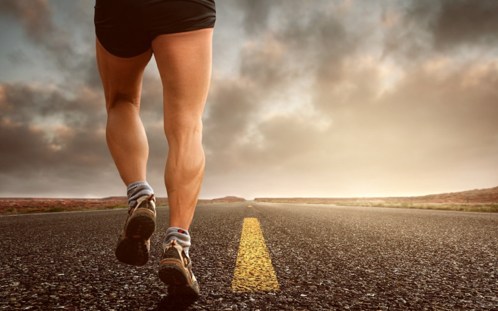 Piernas de un corredor con tenis para correr en una carretera, durante un entrenamiento de resistencia y fitness al aire libre.