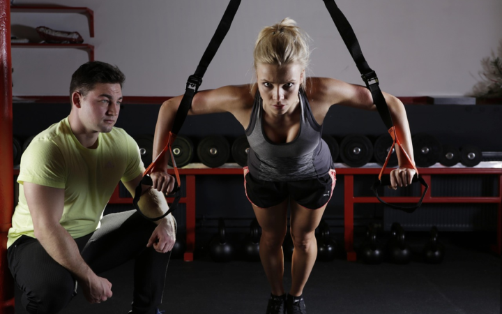 Mujer atlética y elegante haciendo levantamiento de pesas con mancuernas y discos de peso, en un entrenamiento de fuerza y fitness.