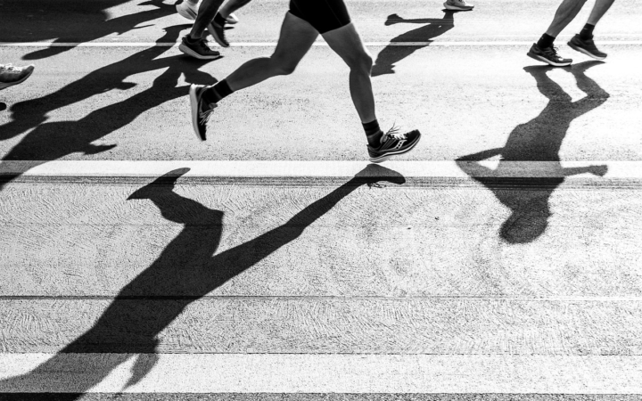Corredores de maratón en una carrera en blanco y negro, con las piernas en movimiento sobre el asfalto y su sombra visible.