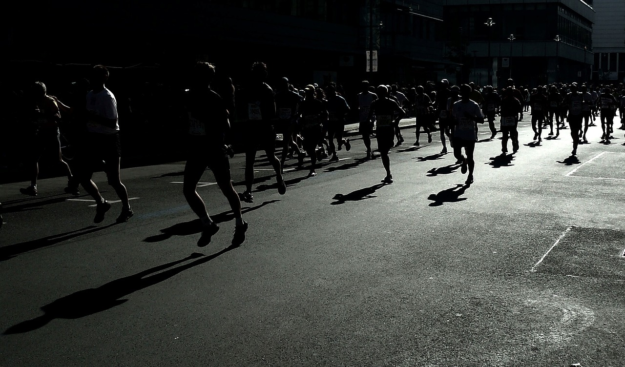Corredor de maratón en blanco y negro, con contraluz y sombras marcadas, durante una competencia deportiva de resistencia.