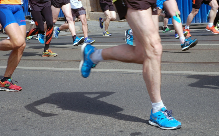 Persona corriendo en una carrera deportiva por la ciudad, con énfasis en pies y músculos de las piernas, relacionada con la salud.