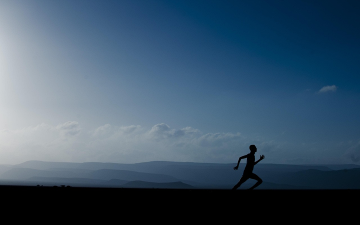 Silueta de un hombre corriendo al aire libre, con montañas y cielo nublado de fondo.