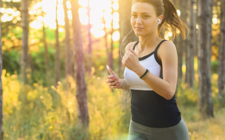 Mujer joven haciendo ejercicio, corriendo con audífonos y su celular, en un estilo de vida activo y saludable.