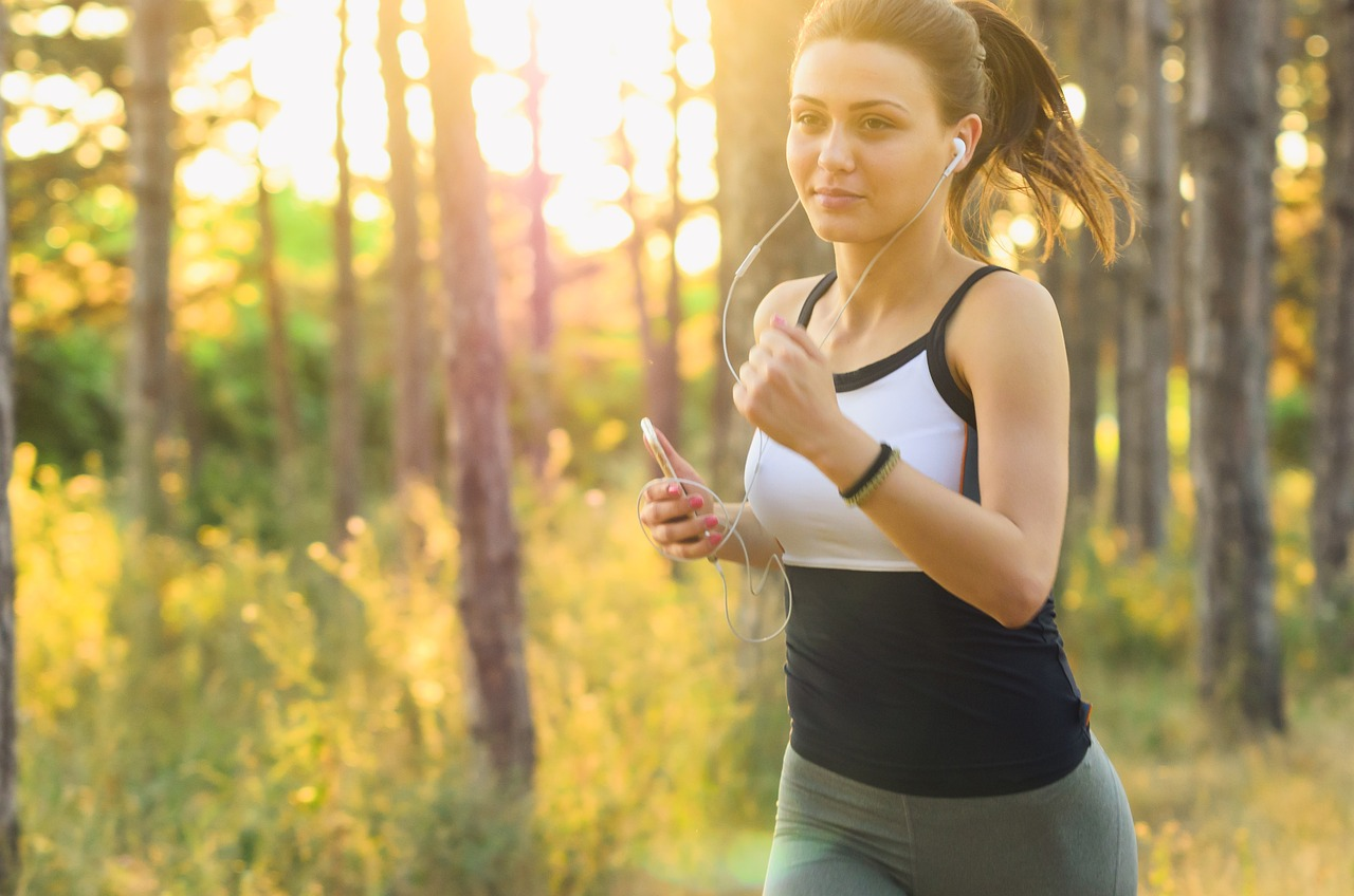 Mujer joven haciendo ejercicio, corriendo con audífonos y su celular, en un estilo de vida activo y saludable.