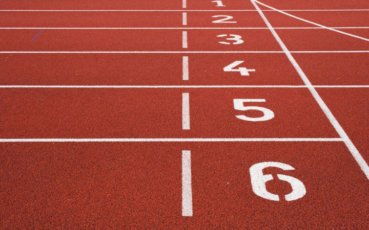 Pista de atletismo con carriles marcados por líneas y números, lista para la salida de una carrera en el estadio.