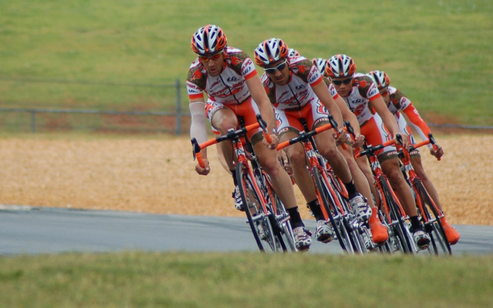 Grupo de ciclistas en una carrera de bicicletas, en acción y a alta velocidad, durante una competencia deportiva en equipo.